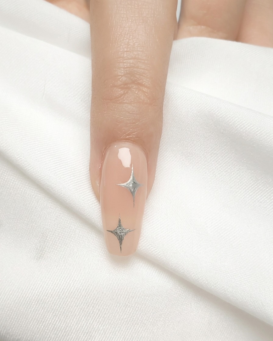 Ein Nagelpinsel trägt eine dünne Schicht nudefarbenes Gel auf einen Naturnagel auf.