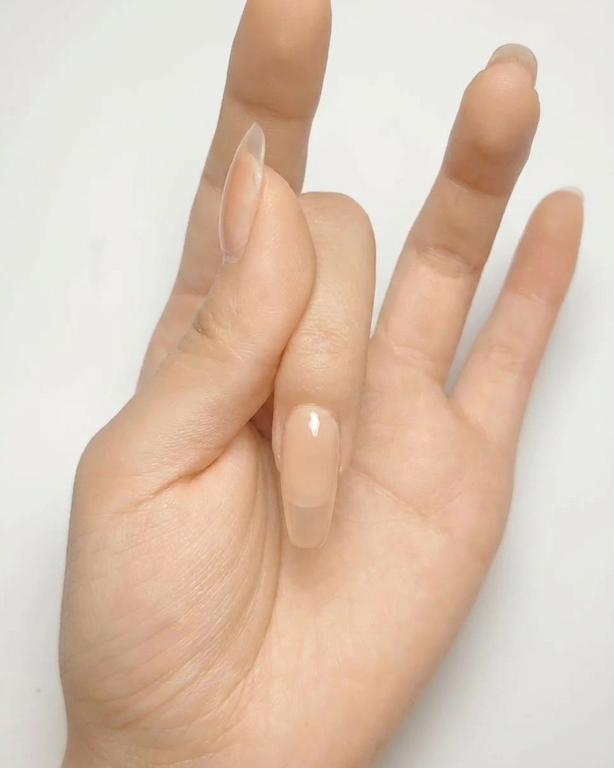 Nahaufnahme eines nudefarbenen Nagels mit einem silbernen Kreuz auf der Oberfläche.