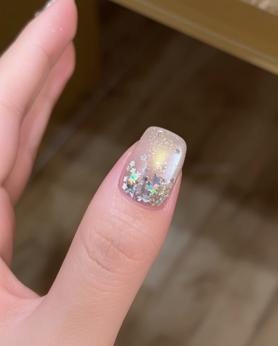 Nahaufnahme eines Fingers, bei dem große silberne sternförmige Pailletten mit einem feinen Pinsel auf einen gelbeschichteten Nagel platziert werden.