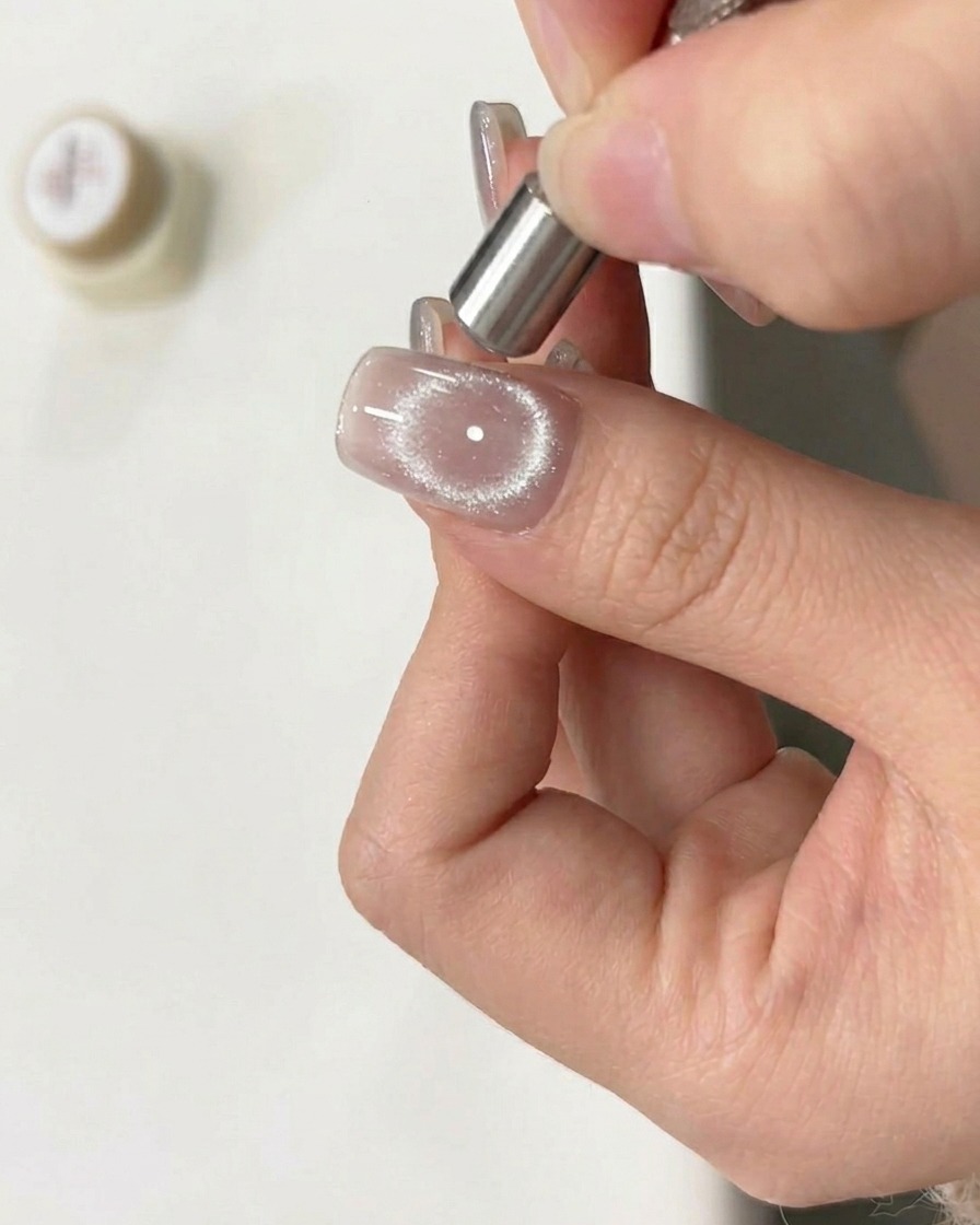 Ein Magnet-Tool wird in kreisenden Bewegungen über den feuchten Cat-Eye-Gel-Nagel gehalten, um einen Ring-Effekt zu erzeugen.