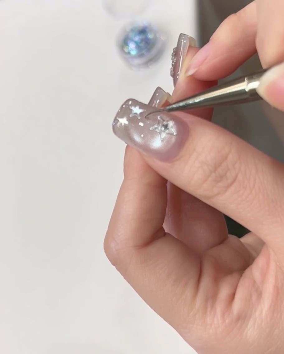 Eine Hand wird unter einer UV-Lampe positioniert, um den mit Sternen verzierten Nagel auszuhärten.