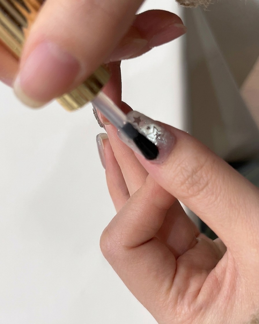 Ein Pinsel trägt einen glänzenden Top-Coat über einen Nagel mit Stern-Glitter auf.