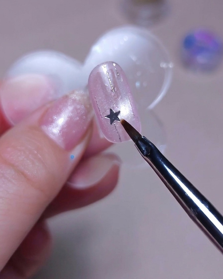 Ein feiner Pinsel platziert eine kleine silberne Stern-Paillette auf einem Nagel.