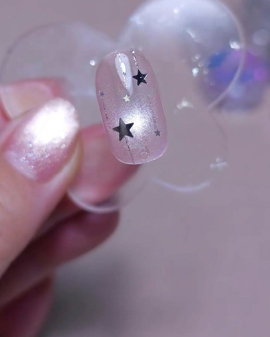 Ein Pinsel trägt eine finale Schicht klaren glänzenden Top Coat über einen mit vertikalen Linien und silbernen Sternen dekorierten Nagel auf.
