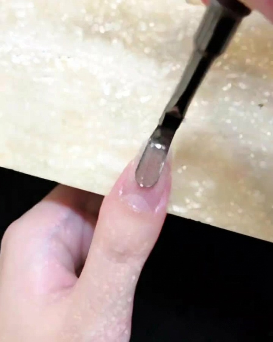 Eine Nahaufnahme, wie ein Nagelpinsel braunes Cat-Eye-Gel auf einen vorbereiteten Fingernagel aufträgt.