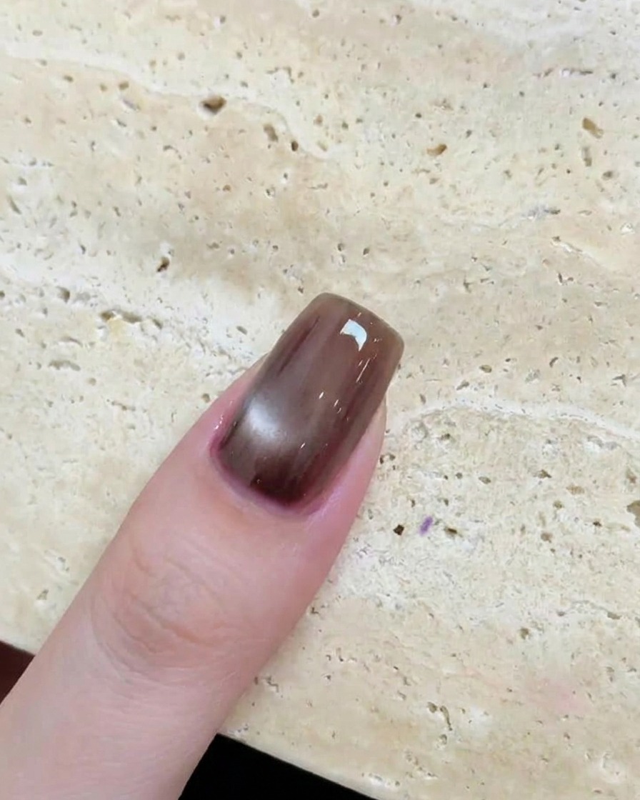 Eine Nahaufnahme eines glänzenden braunen Nagels mit einem kreisförmigen, reflektierenden Cat-Eye-Effekt nach dem Aushärten.