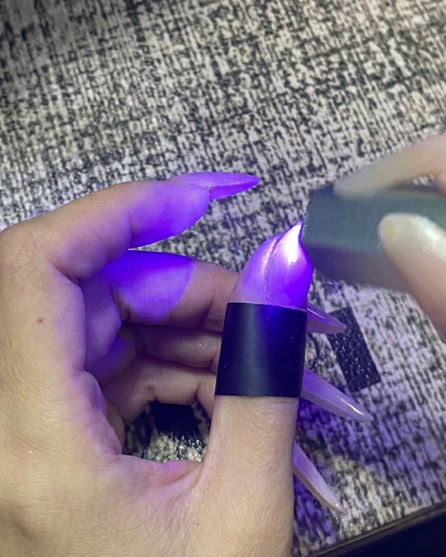 Ein Finger in einer tragbaren UV-/LED-Nagellampe bei eingeschaltetem Licht.
