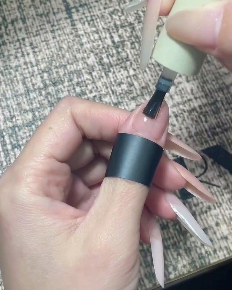 Ein Nagelpinsel trägt präzise klaren Top Coat auf die obere Hälfte des nude lackierten Nagels auf.