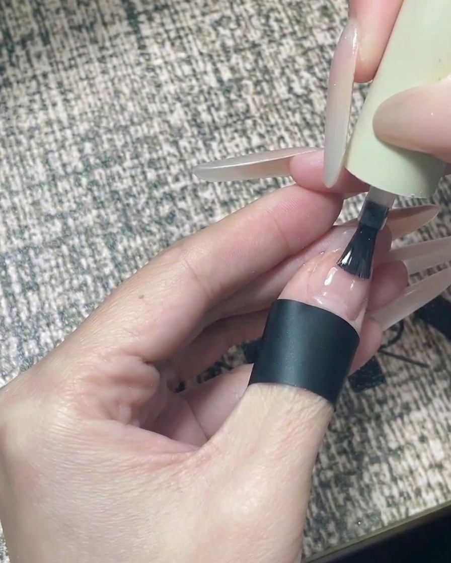 Ein Pinsel trägt klaren, glänzenden Top Coat auf ein fertiges Nageldesign mit Sternen auf.