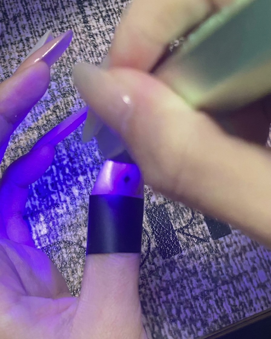 Ein Daumen mit Stern-Nail-Art härtet unter einer lila Mini-UV-/LED-Lampe aus.