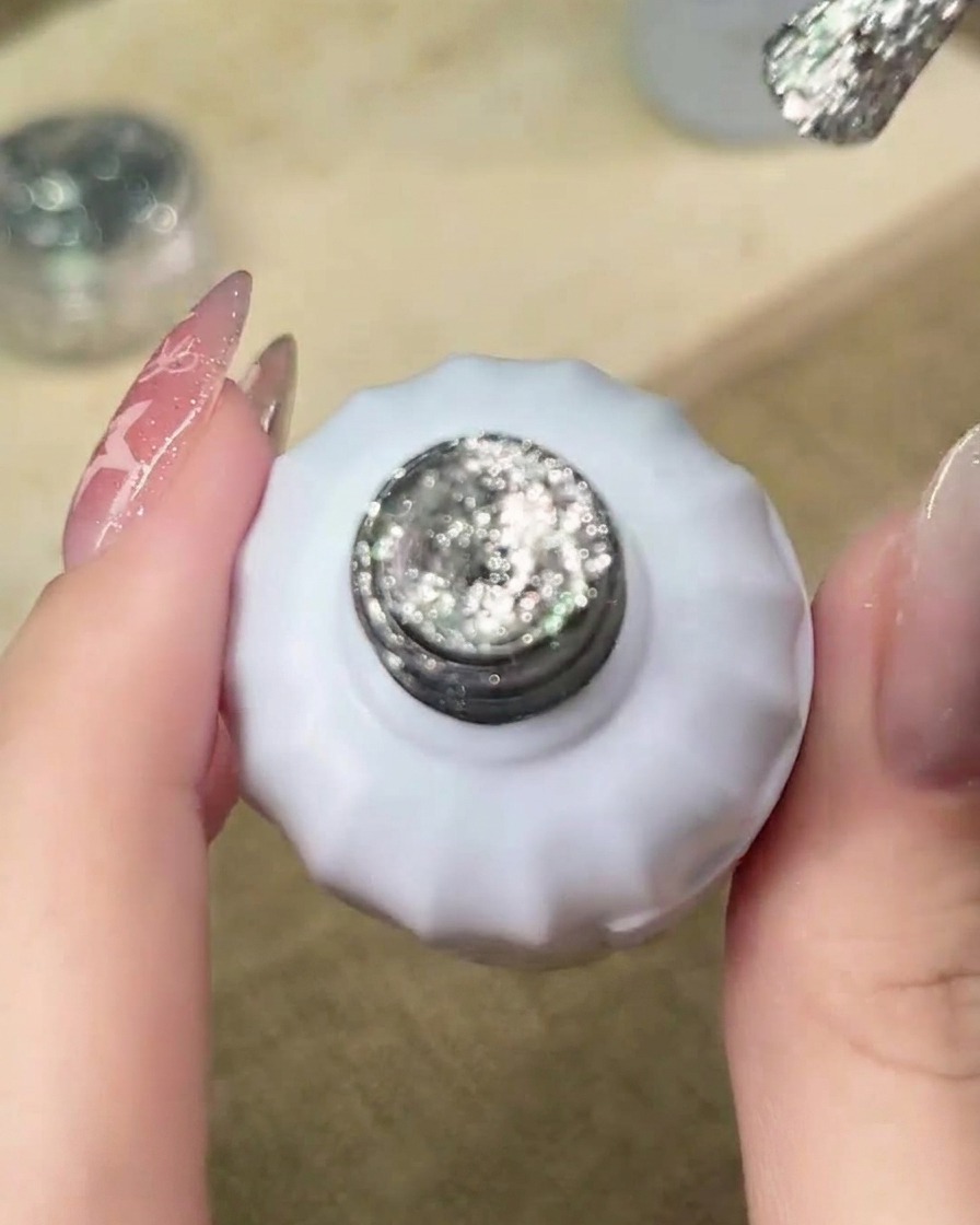 Ein Pinsel trägt silbernes Glitzer-Gel auf die freie Nagelspitze auf und beginnt den Verlaufsprozess.