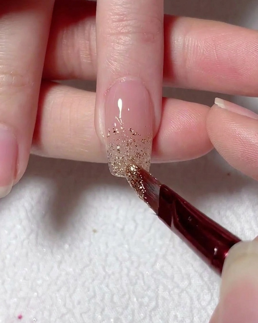 Ein feiner Pinsel verblendet silbernen Glitzer von der Nagelspitze aus nach oben für einen Ombré-Effekt.