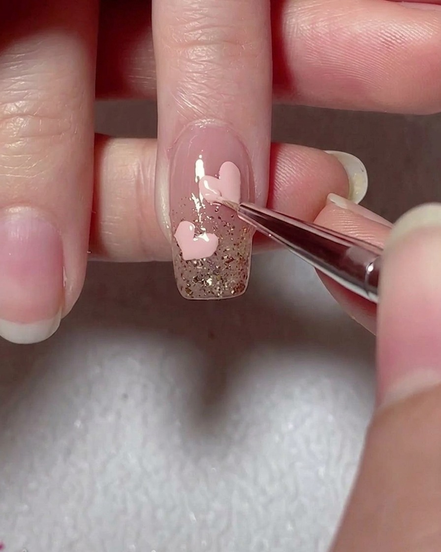 Ein Liner-Pinsel verfeinert die Ränder eines pinken Gelherzens auf einem mit Glitzer akzentuierten Nagel.