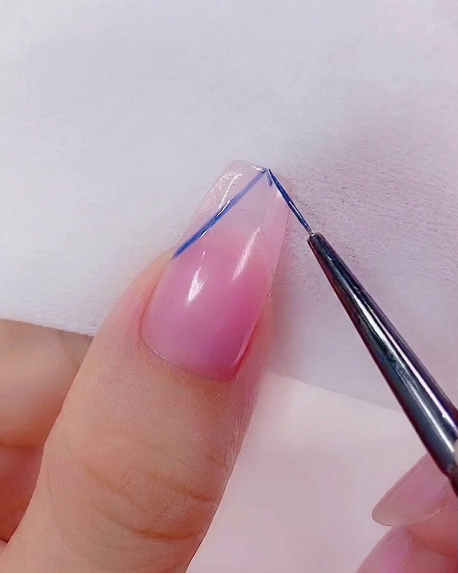 Eine Nahaufnahme eines Liner-Pinsels, der die Kanten eines blauen Herzdesigns auf dem Nagel verfeinert.