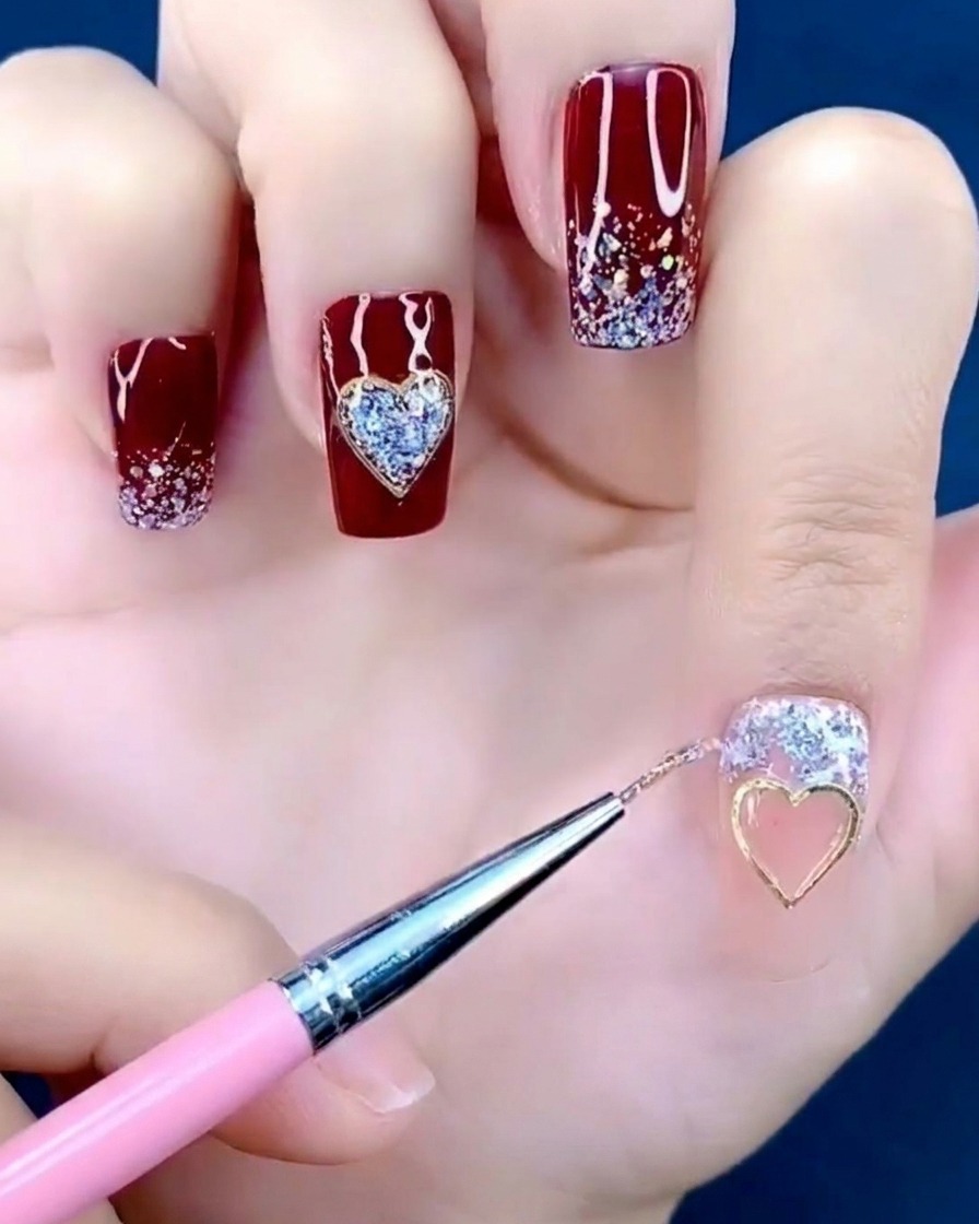 Pinzette, die einen kleinen Metall-Herz-Charm hält und ihn auf die Mitte eines Fingernagels setzt.