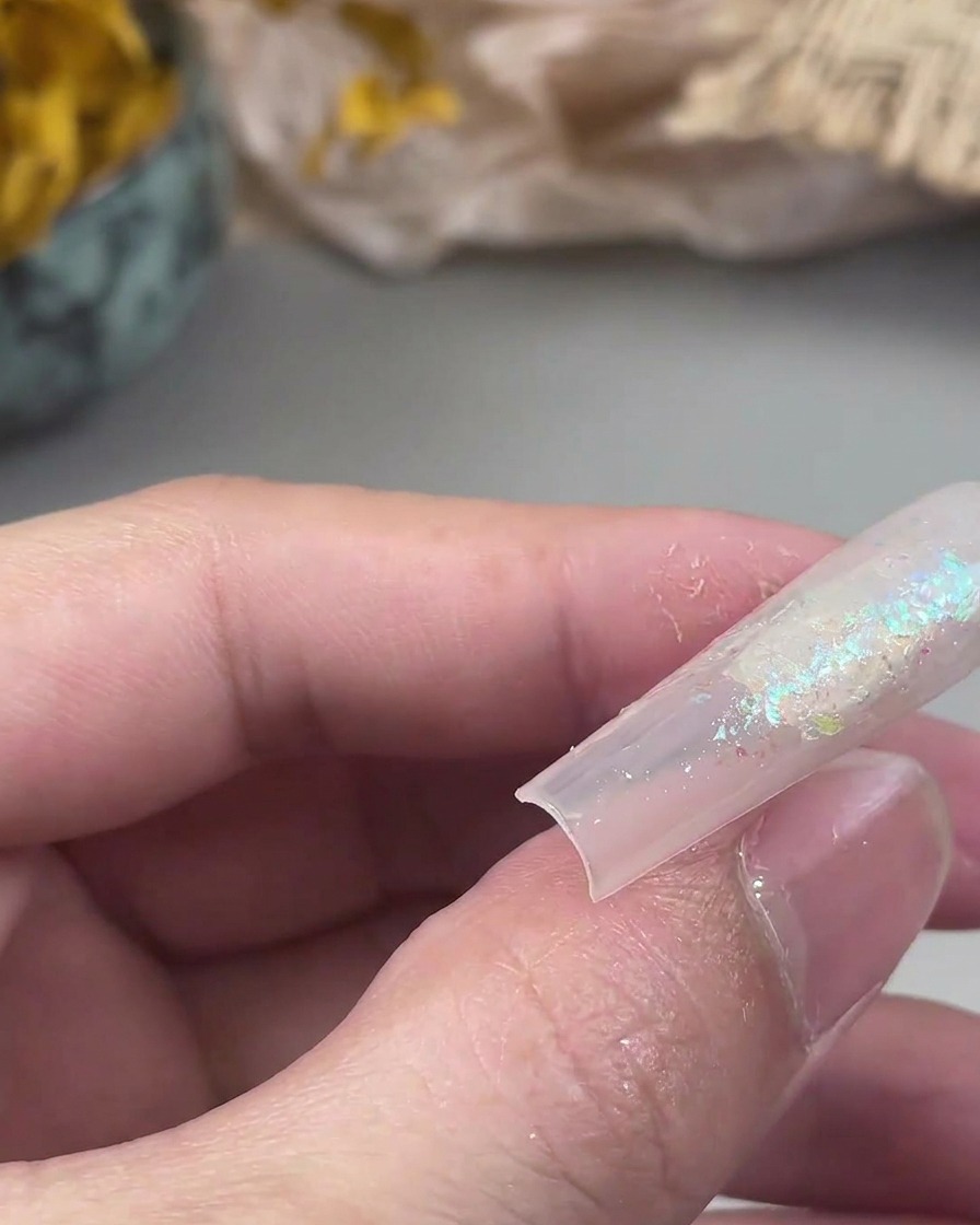 Ein kleiner Flachpinsel drückt lose Glitzerpartikel auf eine klebrige Geloberfläche auf einem Nagel fest.