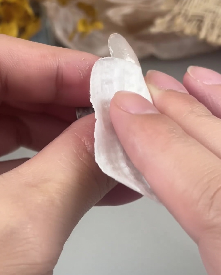 Eine Hand benutzt ein fusselfreies Tuch, um die Oberfläche eines ausgehärteten Gelnagels zu reinigen.