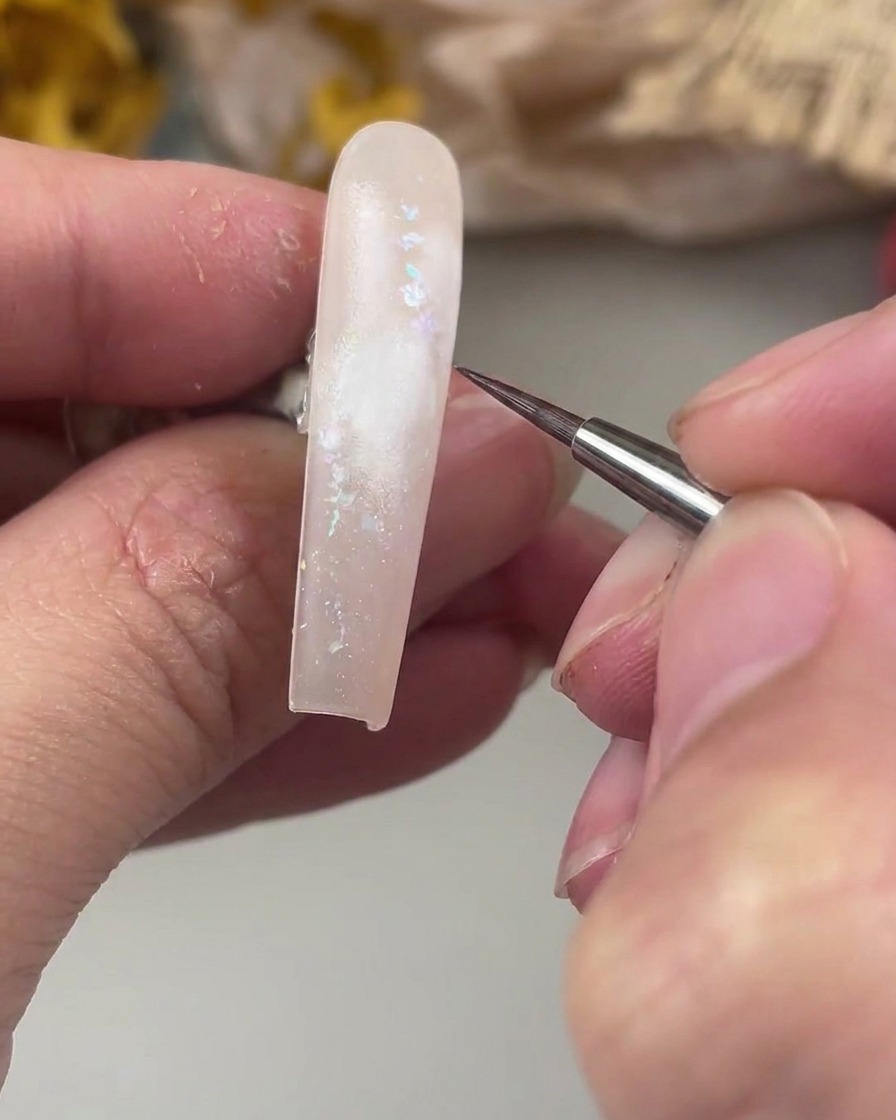 Ein feiner Linerpinsel schwebt über dem weiß bemalten Bereich auf dem Nagel, bereit, das zarte Aquarell-Rosenzentrum zu malen.