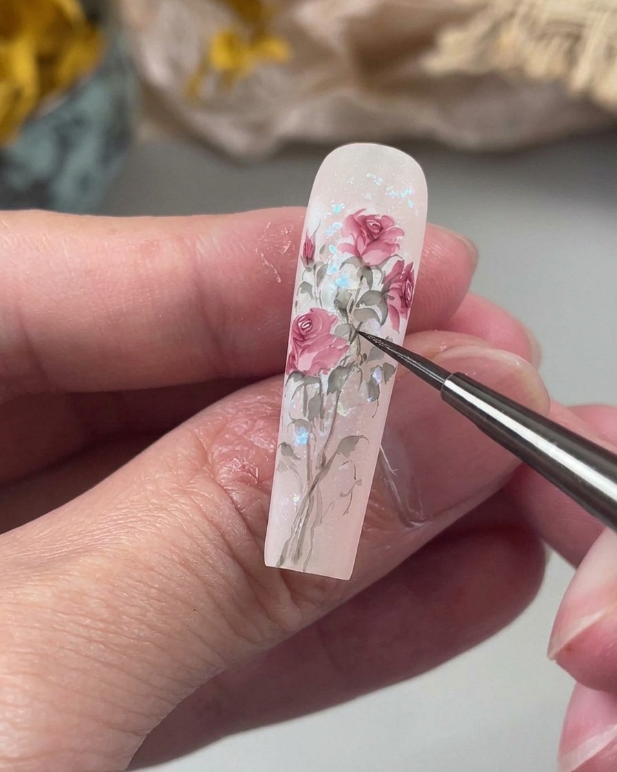 Ein feiner Detailpinsel zeichnet zarte, leicht geschwungene Stiele in einem sanften Grünton, die gemalte florale Elemente auf dem Nagel verbinden.