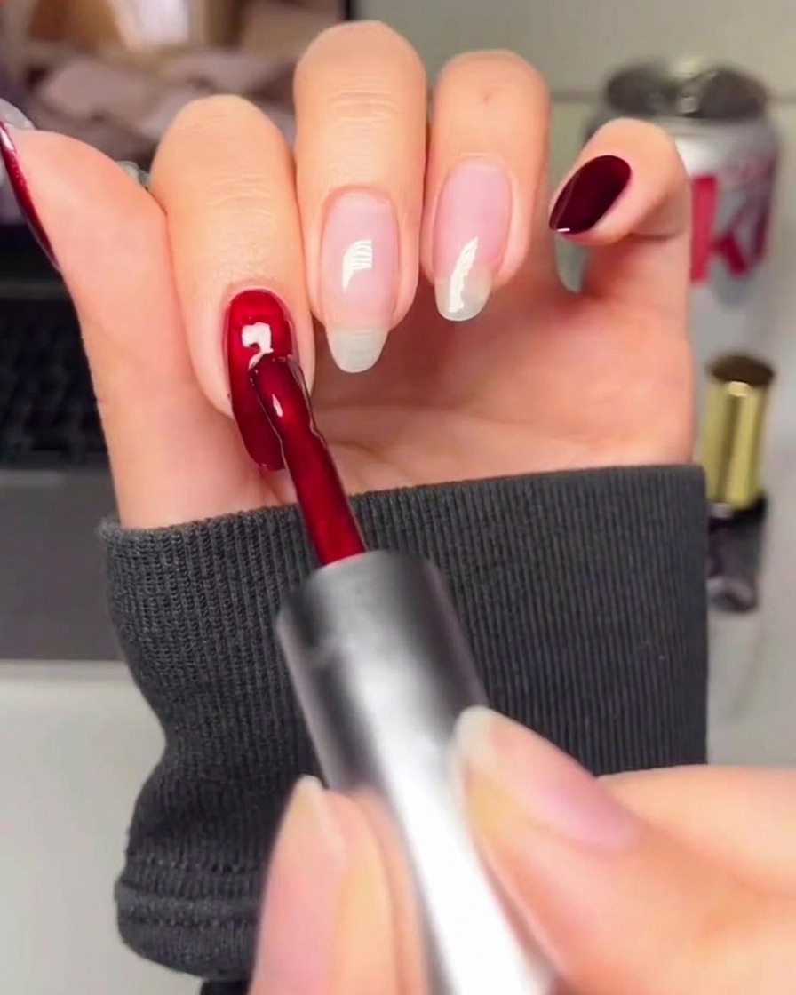 Ein Nagelpinsel trägt ein sattes, tiefes Rot auf eine vorbereitete Nageloberfläche auf.