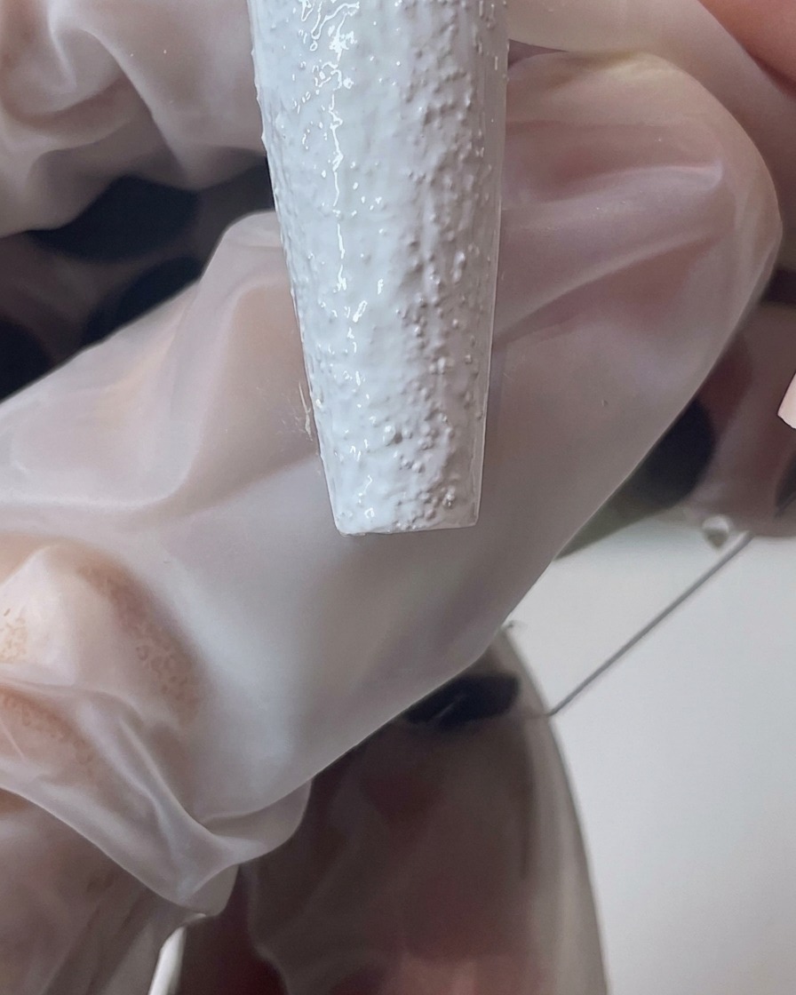 Nahaufnahme eines Pinsels, der weißes Sandgel modelliert, um einen dickeren, strukturierten Nagelrand zu erzeugen.