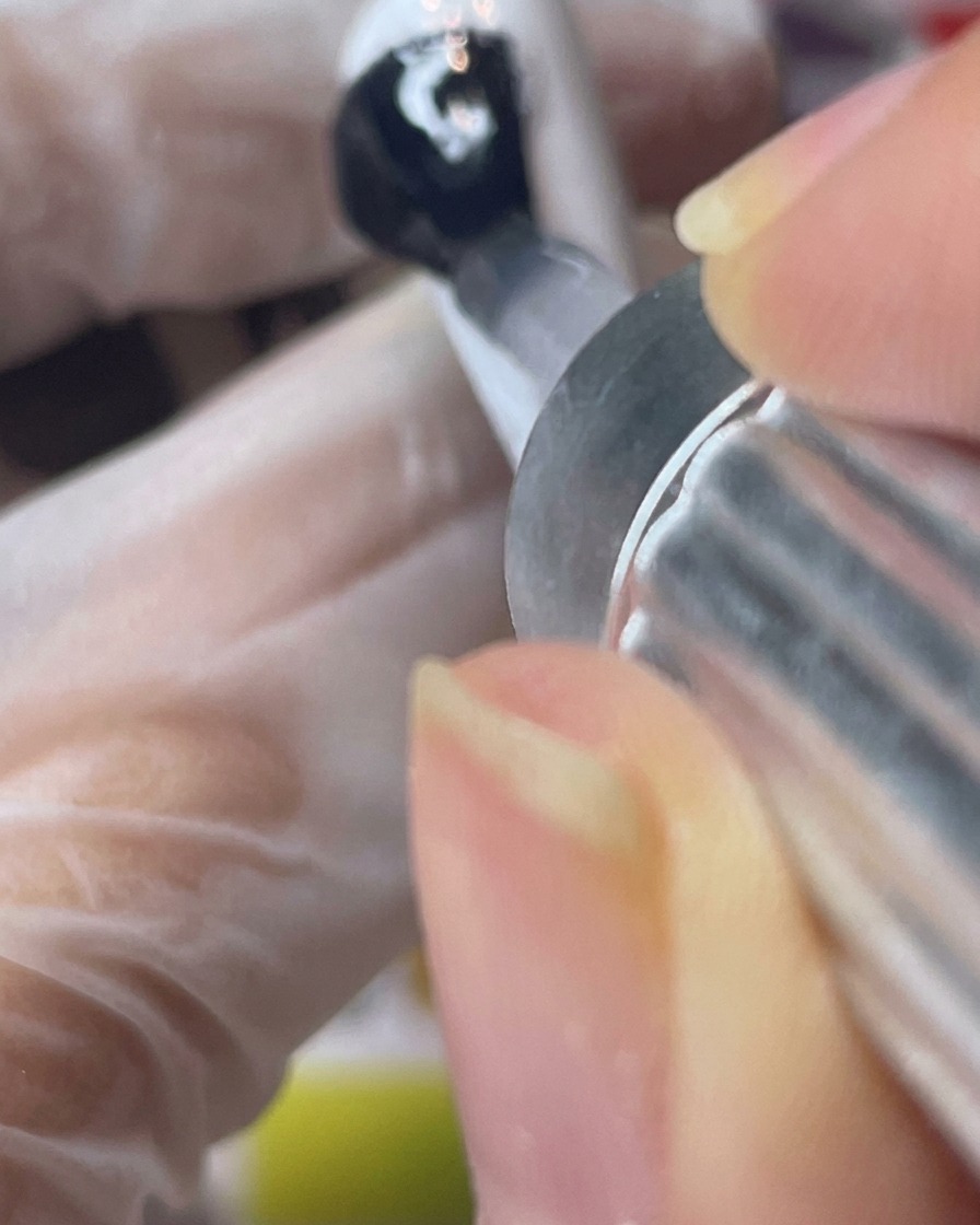 Auftragen eines klaren, matten Top Coats über einen weiß lackierten Nageltip.