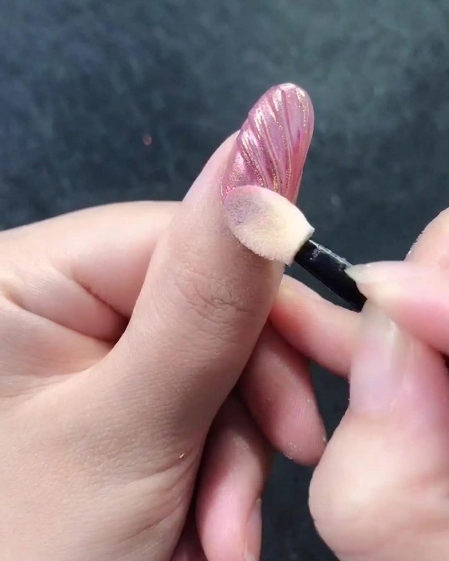 Ein Schwammapplikator poliert Chrom-Puder in die Rillen eines Muschelnageldesigns.