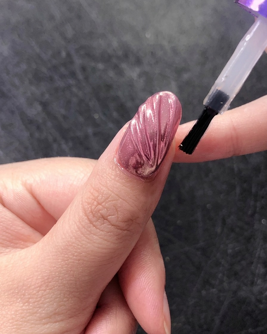 Ein Pinsel trägt einen letzten glänzenden Top Coat über einem Chrom-Muschelnageldesign auf.
