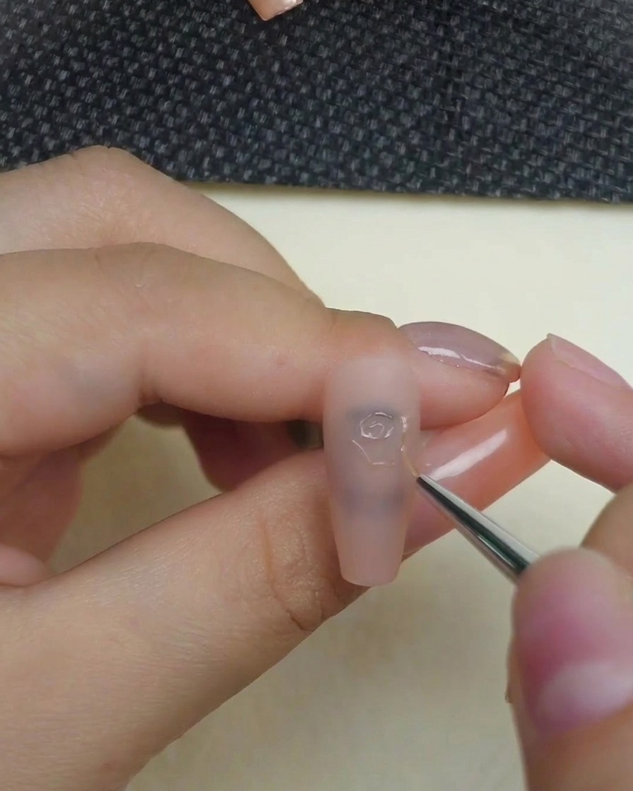 Detailaufnahme eines Pinsels beim Zeichnen der zentralen Rosenwirbel mit 3D-Gel auf einem matten Nude-Nagel.
