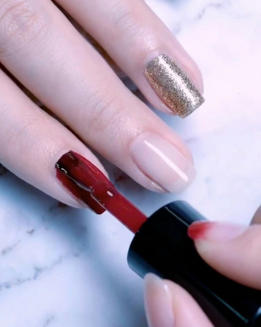 Ein Pinsel trägt eine zweite Schicht Goldglitzer-Gel auf den Nagel auf, wodurch ein sattes, funkelndes Finish entsteht.