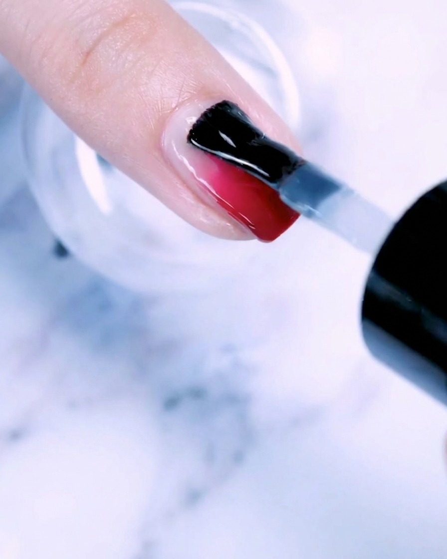 Ein Pinsel trägt eine klare Schicht Basisgel auf einen Fingernagel mit Roségold-Verlauf auf.