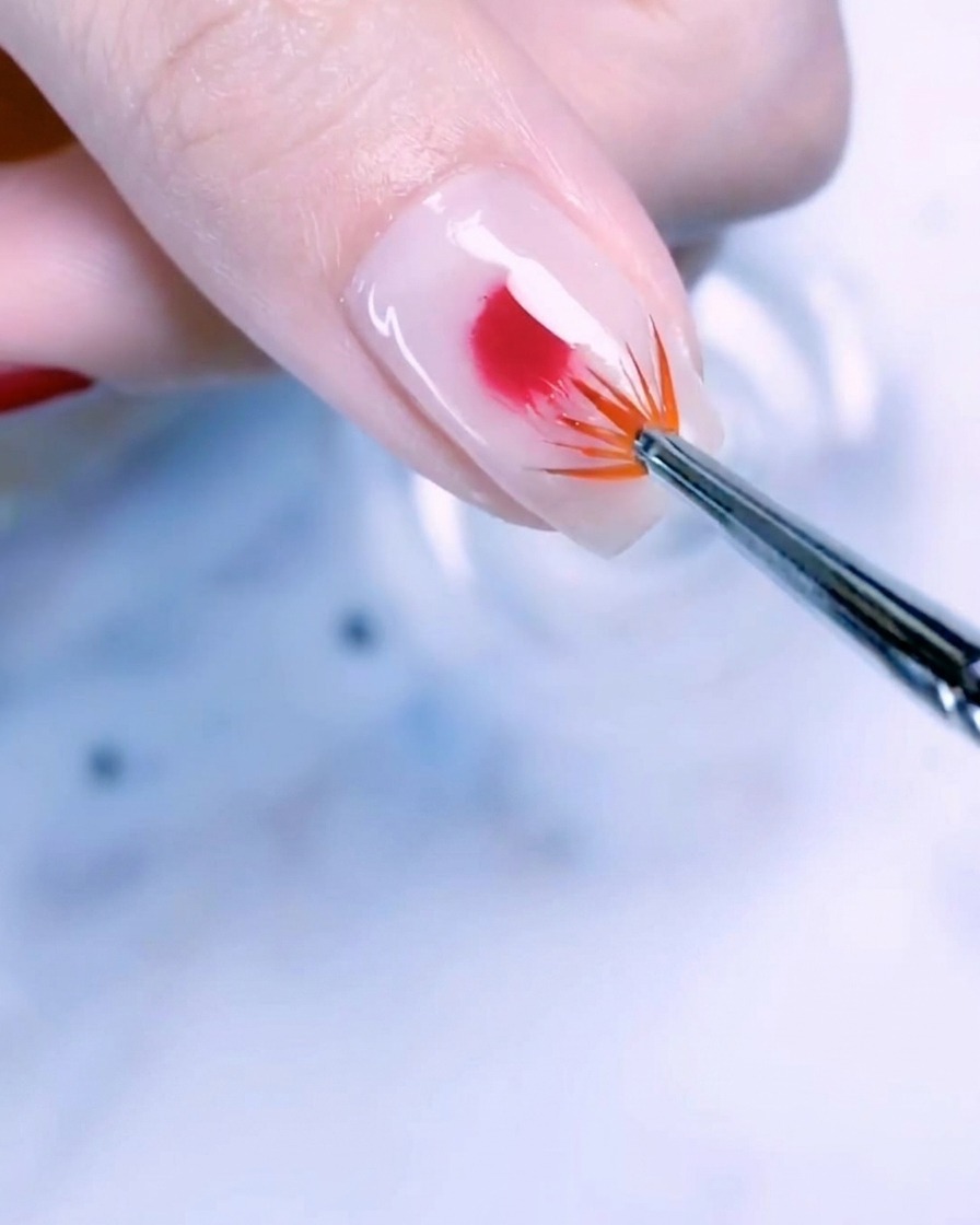 Nahaufnahme eines Daumennagels mit milchiger Basis, auf dem ein Roségold-Punkt mit einem Fächerpinsel nach außen verblendet wird.