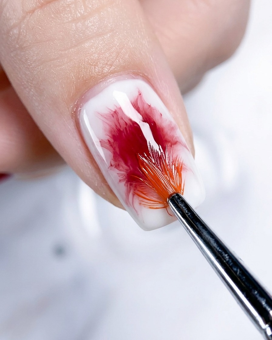 Nahaufnahme eines Daumennagels, bei dem der Roségold-Blush-Effekt mit einem Fächerpinsel weiter verblendet und vertieft wird.