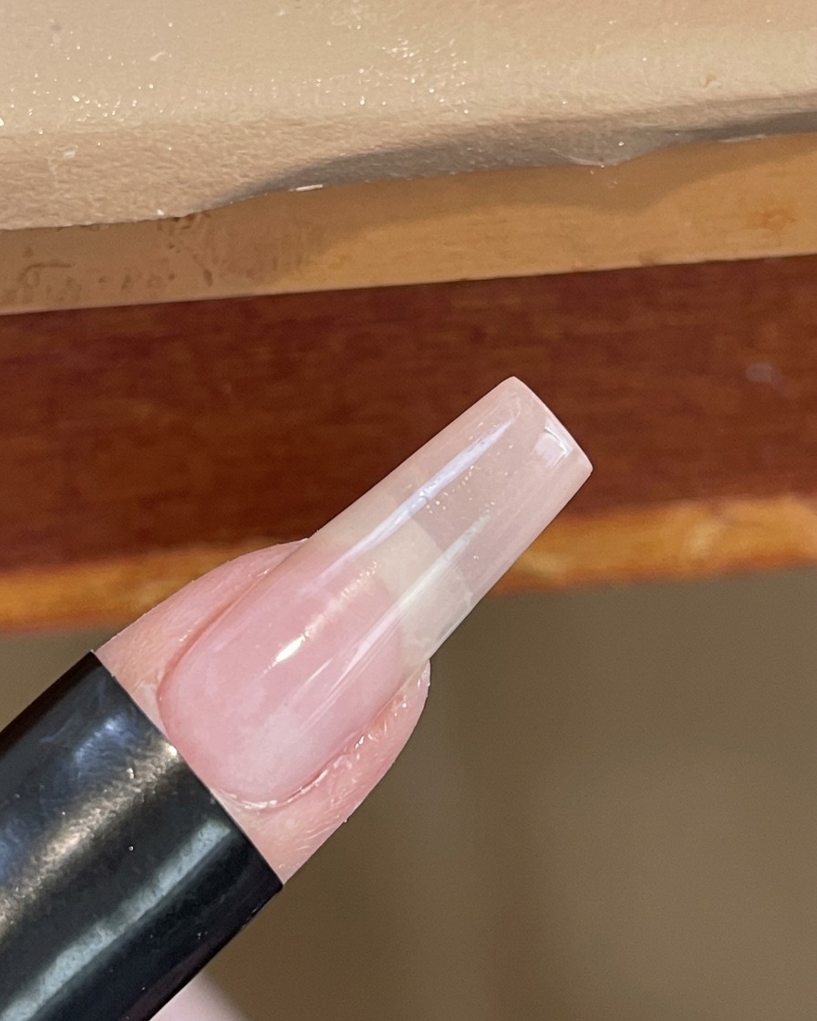 Nahaufnahme eines Nagels, der unter einer kleinen, weißen UV/LED-Handlampe ausgehärtet wird.