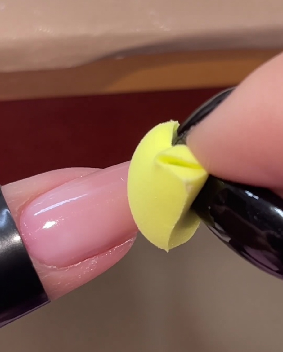 Ein gelber Schwamm-Keil tupft eine zweite Schicht rosa Gel auf die Spitze eines Nagels.