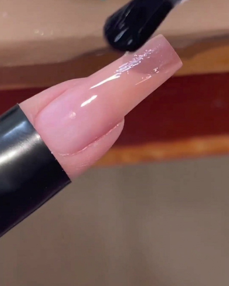 Ein Nagelpinsel trägt einen klaren, glänzenden Top Coat auf einen fertig verlaufenden Nagel auf.