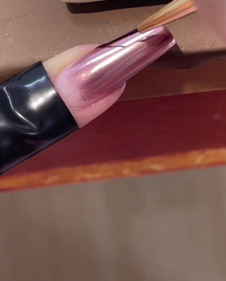 Ein feiner Nailart-Linerpinsel zieht eine klare Linie aus Aufbaugel diagonal über einen Chrome-Nagel.