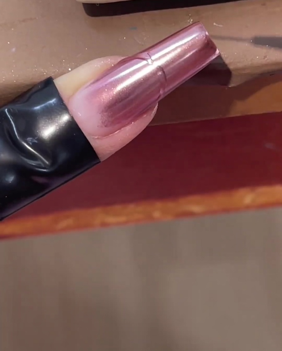 Ein feiner Linerpinsel zeichnet eine erhabene klare Gellinie über einen rosa Chrome-Nagel.