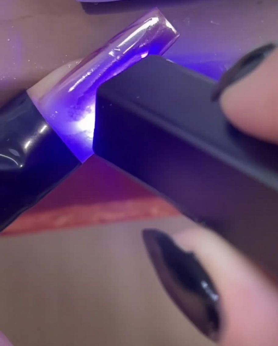Eine Mini-UV/LED-Handlampe härtet klare 3D-Aufbaugel-Linien auf einem Nagel aus.