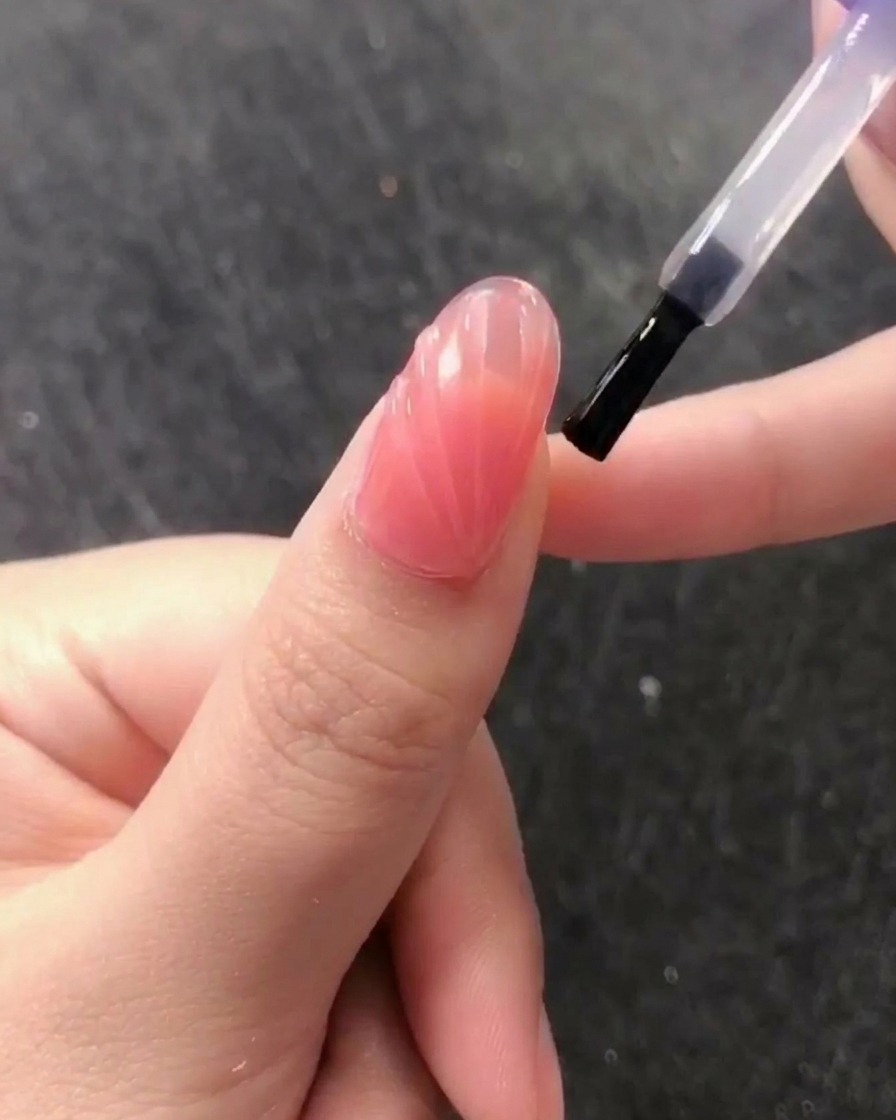 Ein Pinsel trägt einen klaren, glänzenden No-Wipe Top Coat über das strukturierte Muscheldesign auf.