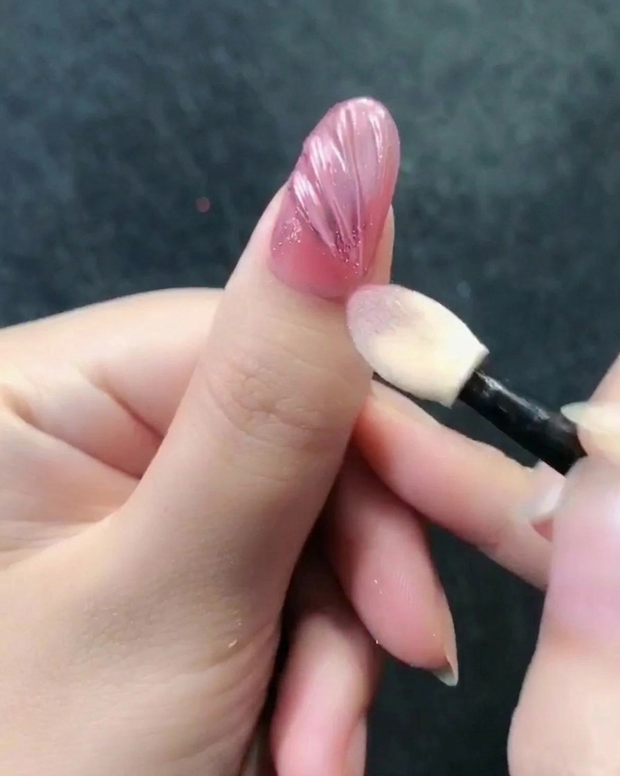 Ein Lidschattenapplikator poliert roségoldenes Chromepuder auf eine strukturierte Nageloberfläche.