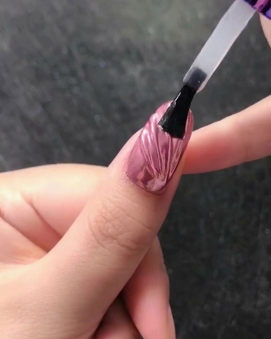 Nahaufnahme eines Wachsstifts, der eine kleine weiße Perle an der Basis eines mit Chrome veredelten Nagels platziert.