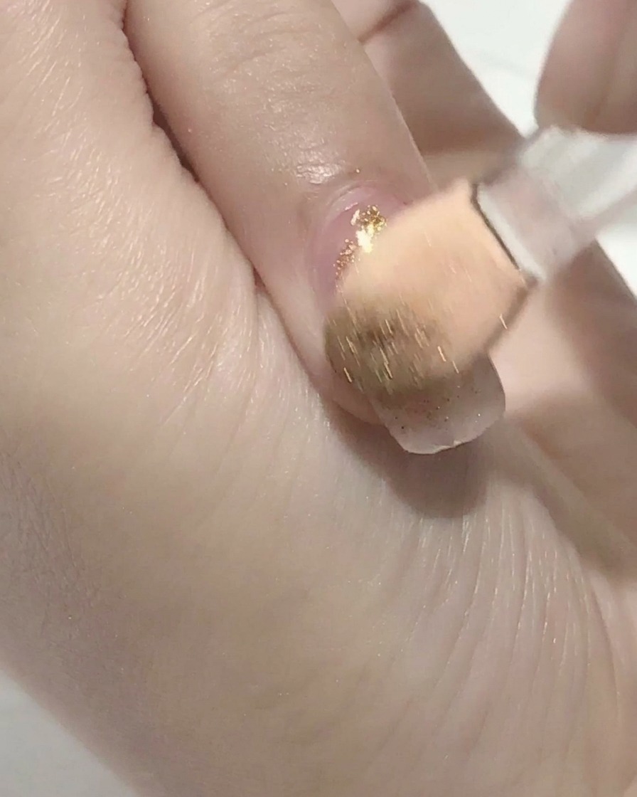 Ein Pinsel trägt klaren Top Coat auf einen rosa Gelnagel auf.