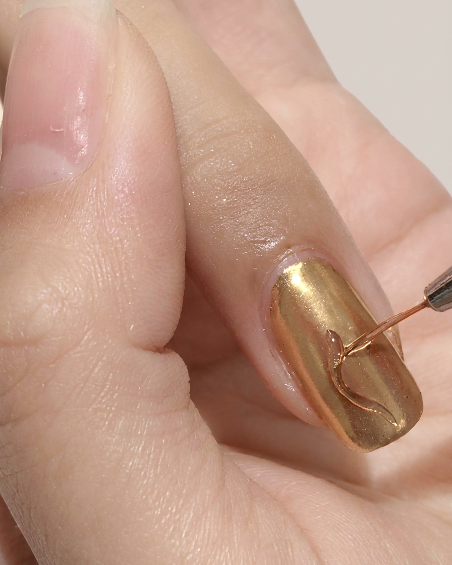 Ein feiner Liner-Pinsel zeichnet eine geschwungene Linie auf einen Gold-Chrome-Nagel.