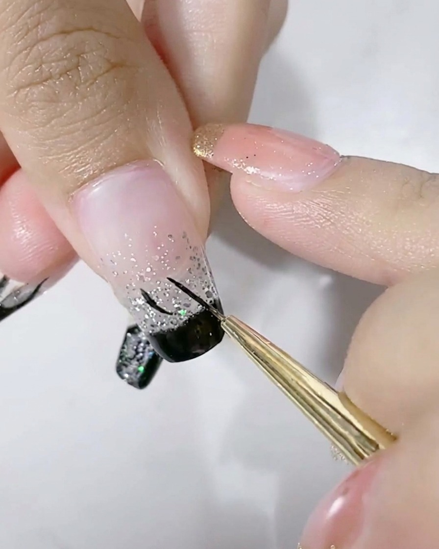 Ein feiner Nail Art Pinsel zeichnet einen schwarzen U-förmigen Bogen auf den silbernen Glitzerbereich eines Fingernagels.