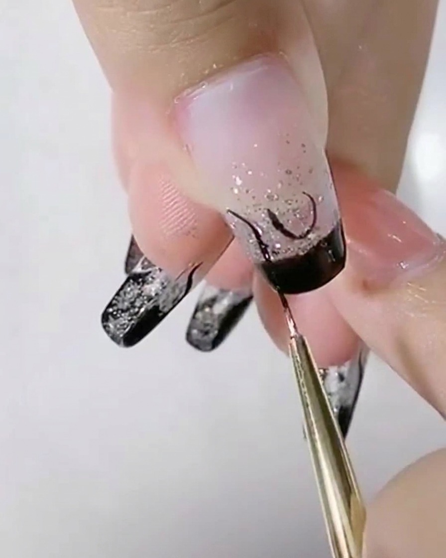 Ein feiner Pinsel fügt neben einer zentralen U-Form schwarze S-förmige Kurven auf einem Glitzernagel hinzu.