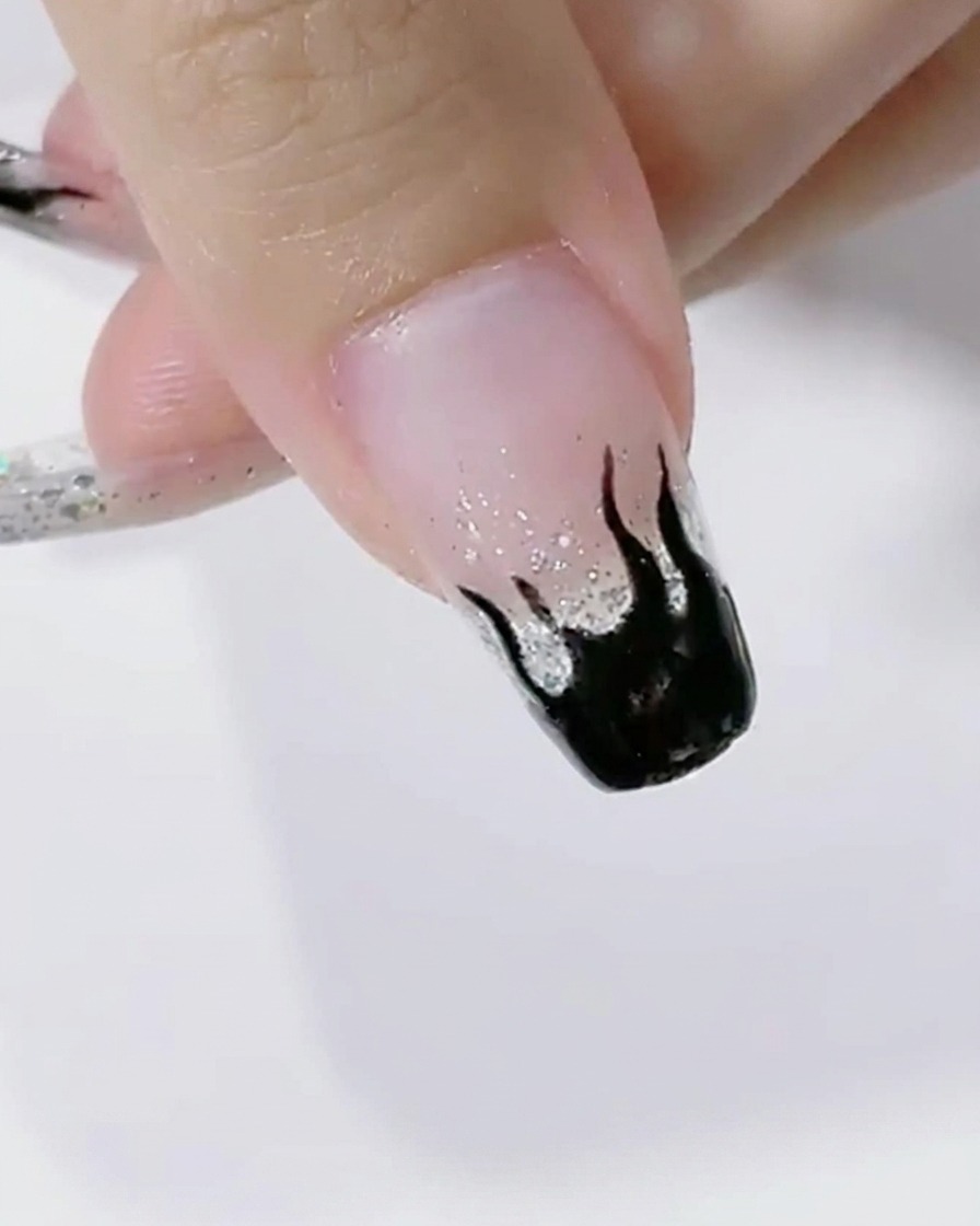 Nägel mit schwarzer Flammen-Nail-Art härten unter dem hellen Licht einer LED-Lampe aus.