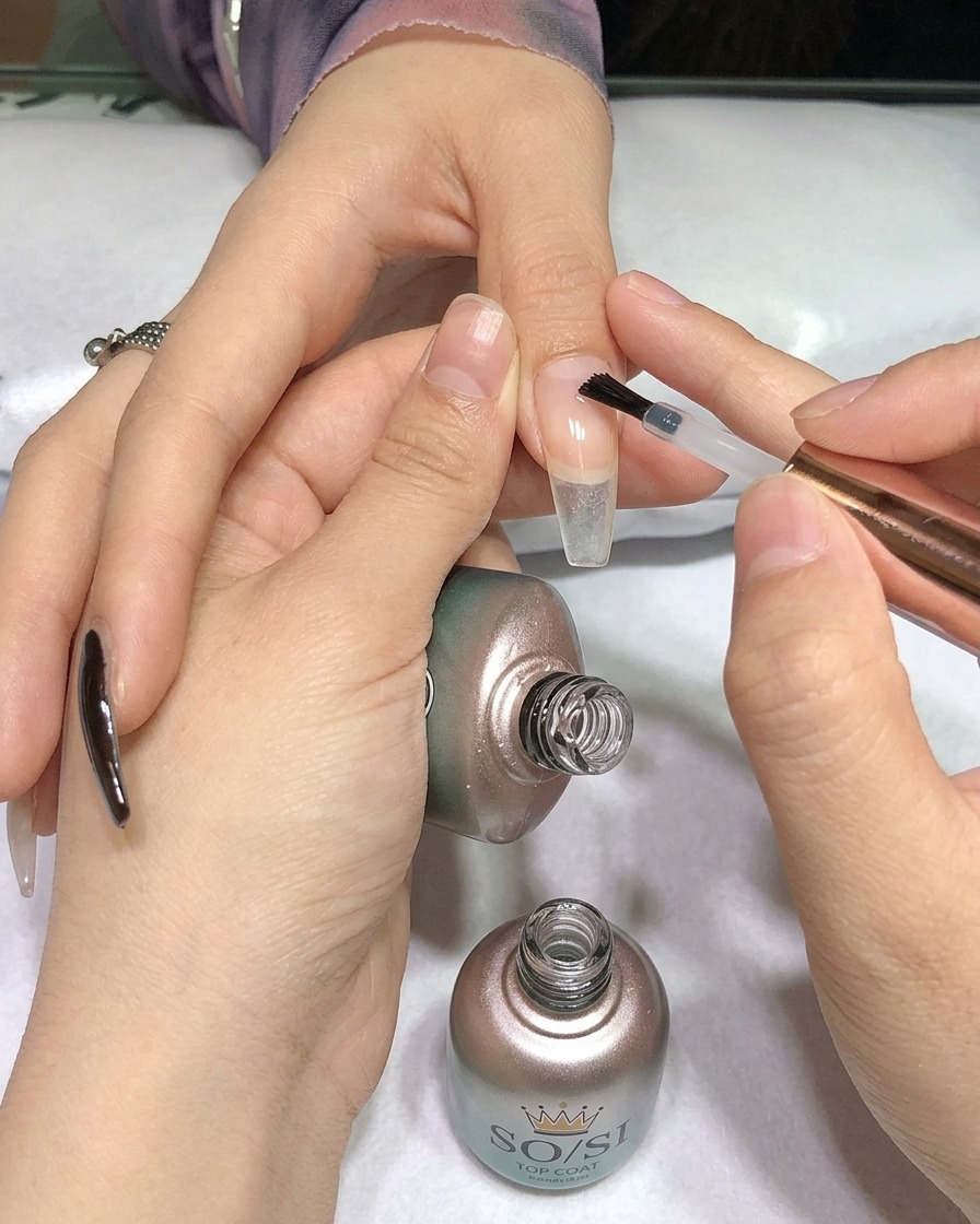 Ein Pinsel trägt klaren Top Coat über einen schwarz lackierten Nagel auf.