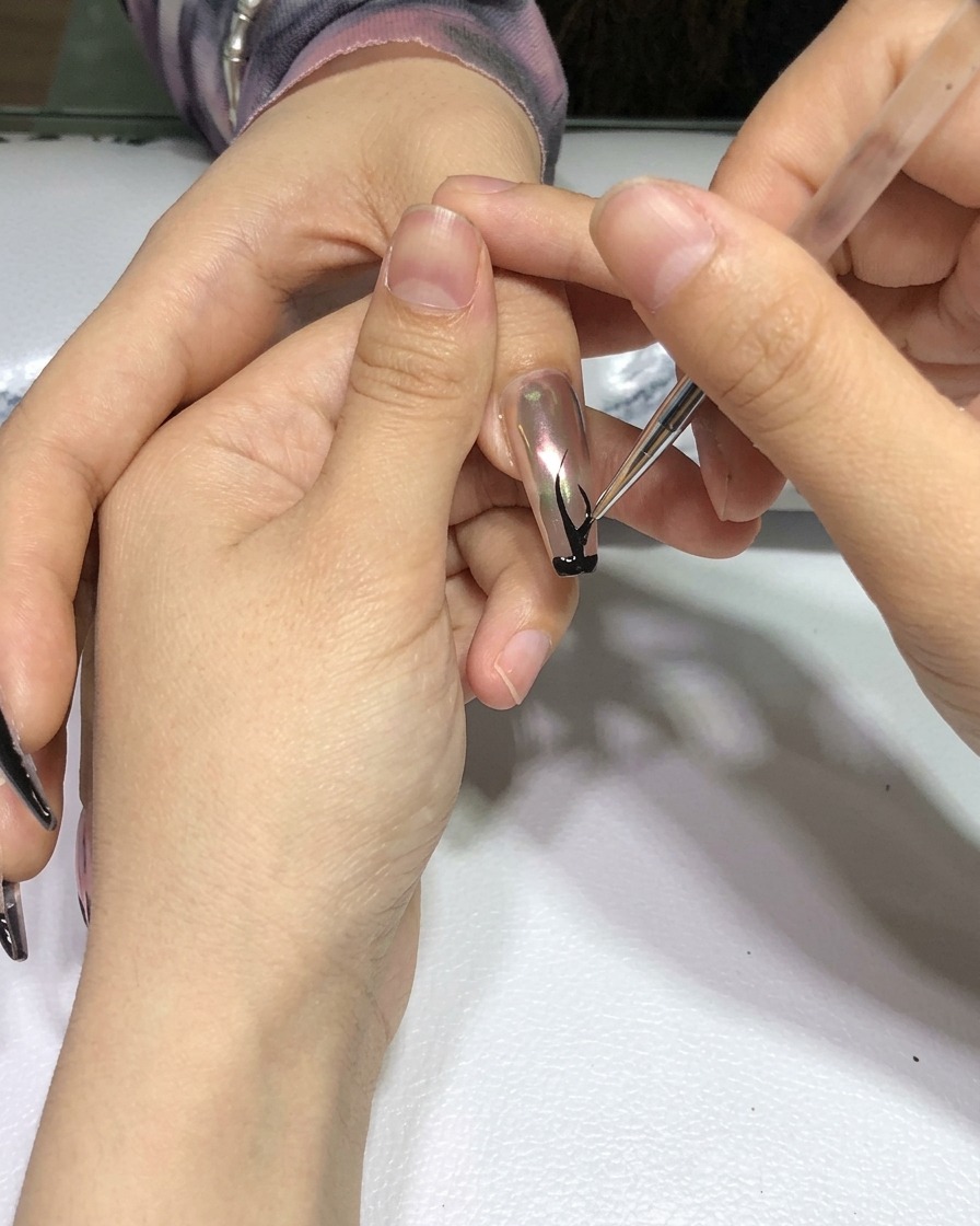 Eine Hand mit fertiggestelltem schwarzen Flammen-Nageldesign in einer professionellen Härtungslampe.