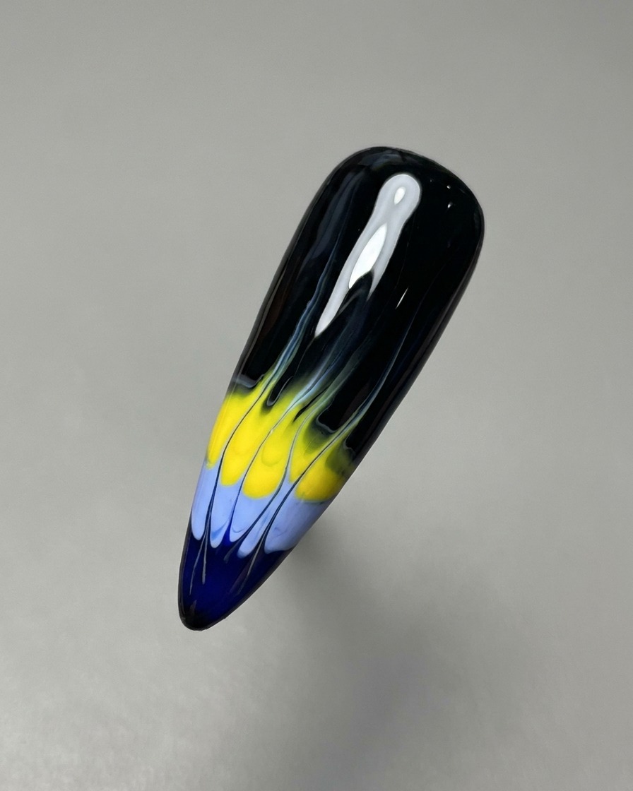 Ein dünner Nail-Art-Liner-Pinsel zieht die blauen und gelben Gel-Farben nach oben, um die Basis des Flammenmusters zu erstellen.